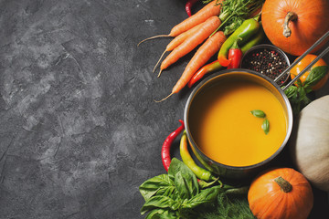 Creamy pumpkins soup with vegetables over black texture.