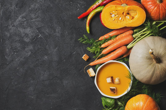 Creamy pumpkins soup with vegetables over black texture
