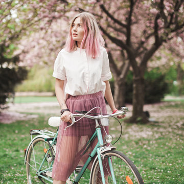 Girl with a pink hair on the bike in the blossoming park