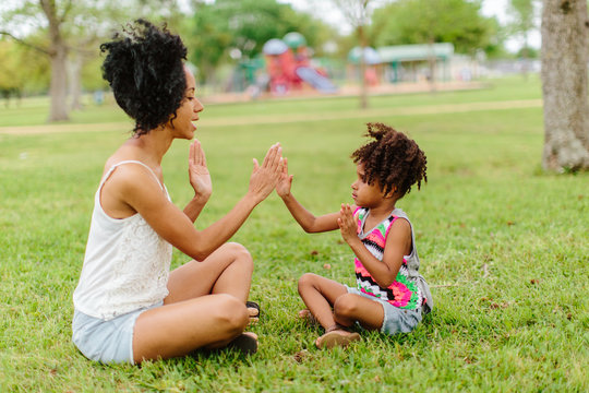 A mother and daughter playing patty cake in the park