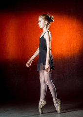 Beautiful young ballerina is dancing in the studio on a dark background. A little dancer. Ballet dancer.