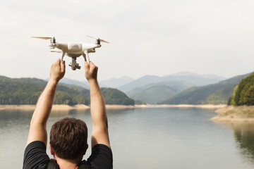 Man is holding white drone near Lake Vidraru at Fagaras Mountains. Romania