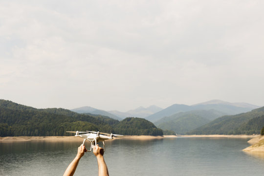 Man is holding white drone near Lake Vidraru at Fagaras Mountains. Romania