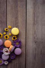 Fototapeta na wymiar Macarons and flowers on the background of a wooden table. Colorful French dessert with fresh flowers. Gradient between purple and yellow. Place for text