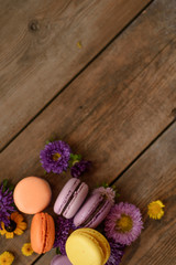 Colorful Macarons and flowers on wooden table background. French dessert with fresh flowers. Top view. Autumn concept