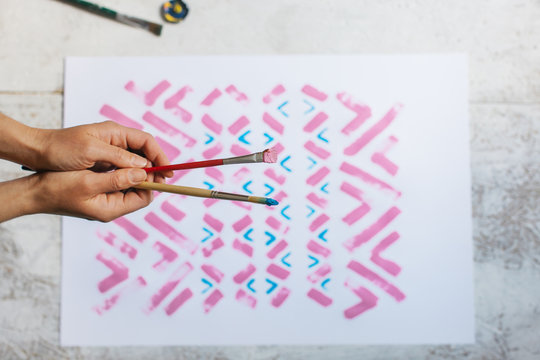 Female Hands Holding Two Paint Brushes Over Pattern Painting