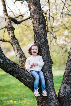 Small girl sitting on a branch of the tree