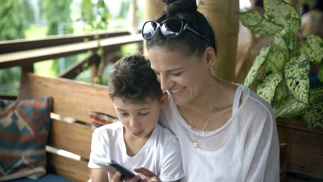 Mother having fun with her son while doing funny photos on smartphone, steadycam shot
