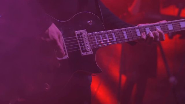 Close up shot of man playing guitar on concert stage. Smoke, strobing red light. Entertainment and art concept