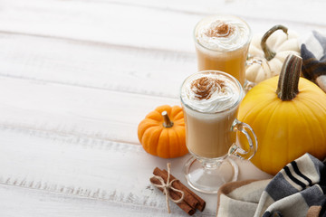 Fall pumpkin spice latte with whipped cream and cinnamon, ornamental pumpkins and warm woolen scarf...