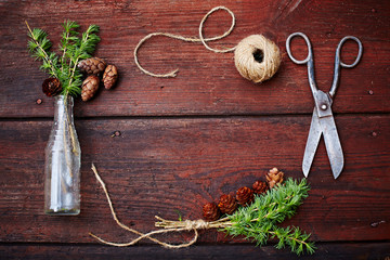 Christmas wooden background.Spruce branches and cones in a vintage bottle, the old scissors and crafty cord. The concept of training sets for Christmas. Top view.