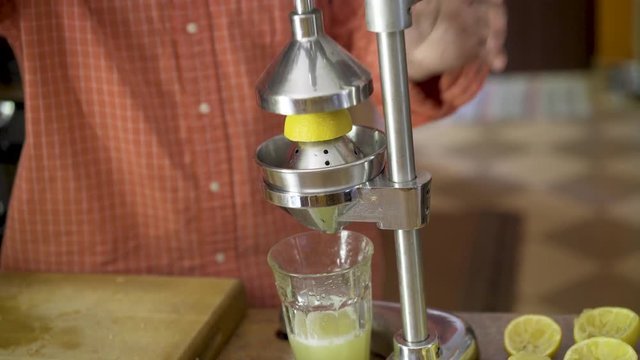 Chef takes fresh cut lemons and puts them into a juicer and presses the juice out of them while camera slides from right to left.