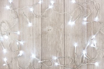 White Christmas lights frame, above view on a light gray wood background