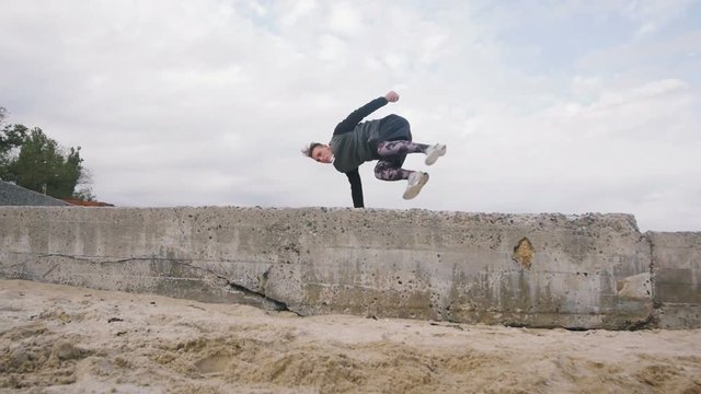Young man doing parkour tricks on the beach near the sea