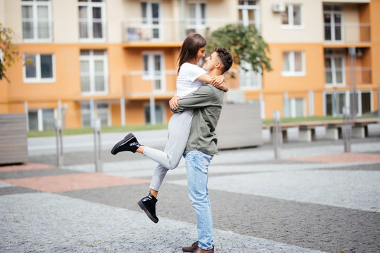 Cute girl jumping to man sunny, summer day. Stylish couple in love hugging and kissing in city street. Relationship, active lifestyle, energy