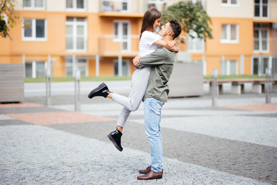 Cute girl jumping to man sunny, summer day. Stylish couple in love hugging and kissing in city street. Relationship, active lifestyle, energy