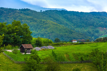 Fototapeta na wymiar A small barn on the field with a wooden fence around on a hill, against a backdrop of a mountain forest. Rural courtyard in the mountains of Valjevo, Serbia.