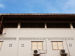 Pale pink white painted continuous townhouse back wall with roof facade, with windows and air compressor box attached, with blue sky white cloud background