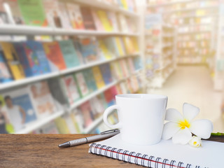White cup of coffee on wooden table over  blur background of bookstore.
