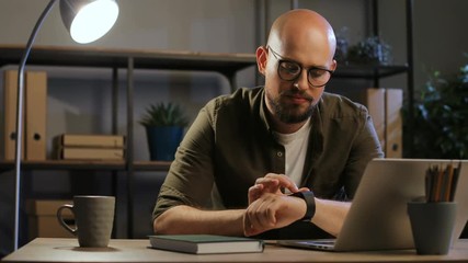 Young serious business man using smart watch during evening time in the stylish office background. - Powered by Adobe