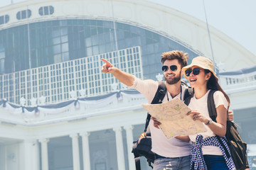Multi ethnic couple look at map while pointing finger in the direction of destination. Travel concept. Honeymoon trip, backpacker tourist, Asia tourism or holiday vacation travel concept.