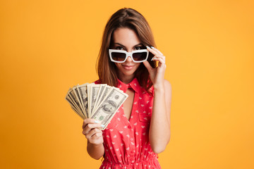 Young attractive brunette woman in sunglasses holding bunch of money, looking at camera