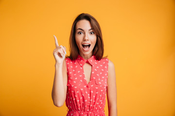 Close-up portrait of amazed pretty young woman in red dress pointing with finger, looking at camera with open mouth