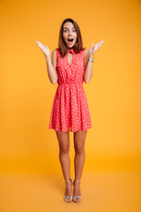 Full length portrait of happy surprised girl in red dress standing with open palms, looking at camera
