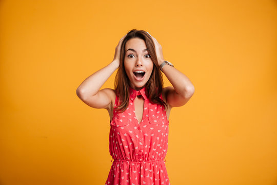 Young Beautiful Woman In Red Dress Holding Her Hands On The Head With Happy Exited Emotional Face, Looking At Camera