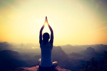 Fototapeta premium young fitness woman meditating on sunrise mountain peak