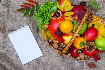 Autumn composition: wicker basket with fruits and vegetables, notebook, top view.