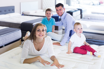 Fototapeta premium Smiling young woman with husband and sons testing mattress in store