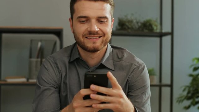 Beautiful businessman with beard using smartphone for surfing the internet in the stylish office.