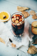 Hot mulled wine in a glass with orange slices, anise and cinnamon sticks, star cookies on vintage wood table. Christmas or winter warming drink with recipe ingredients around
