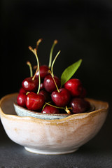 ripe  bright cherry with leaves in a clay bowl on a dark background.Dark Key