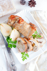 Roll of pork and pears on a white plate with a bottle of wine in Christmas decorations, top view