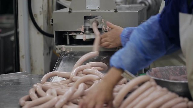 The process of making sausages at a meat-packing plant. Workers in uniform make sausage.