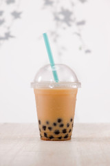 Light brown creamy bubble tea and black tapioca pearls  in plastic cups on table.