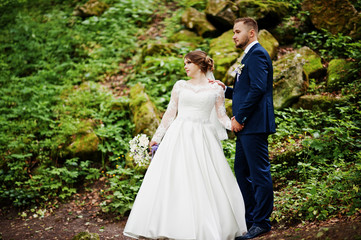 Newlyweds posing with huge rocks on the background in the forest on a wedding day.