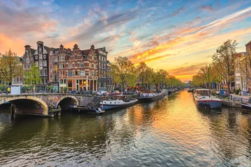 Tuinposter De skyline van de zonsondergangstad van Amsterdam aan de waterkant van het kanaal, Amsterdam, Nederland © Noppasinw
