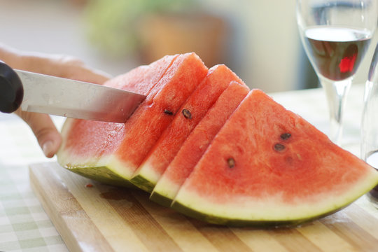 watermelon slices cut with knife on wooden chopping board with red wine glass on the side