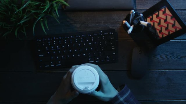 Top down shot of man with cup of tea typing on keyboard