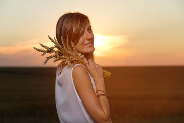 Fototapeta na wymiar Beautiful woman holding wheat and enjoying the sunset in field.