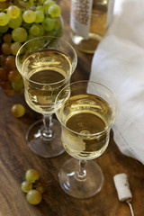 White wine with glass goblets and grape bunches on a wooden background.