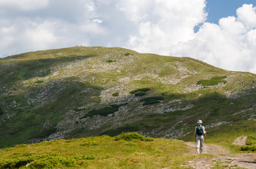 Fototapeta premium A young girl using the Nordic walking poles makes a pedestrian climb on the mountain. A young girl makes a hike on the scrumptious mountain tops of the Ukrainian Carpathian mountains.