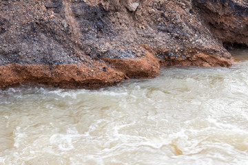 Water flows into gravel, rocks, under the road.