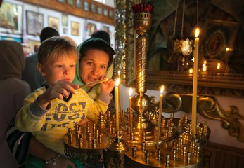 a child with his mother lighting a candle in a church.