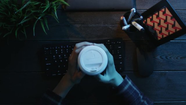 Overhead shot of man drinking coffee and warming up his fingers before typing on keyboard