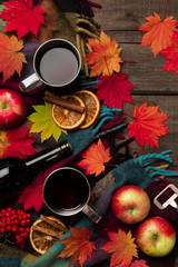 Autumn leaves, two cups of wine, red apples with plaid on old vintage wooden background.