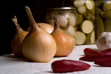 Onions lie on a white cloth among pepper, garlic and pickled vegetables
